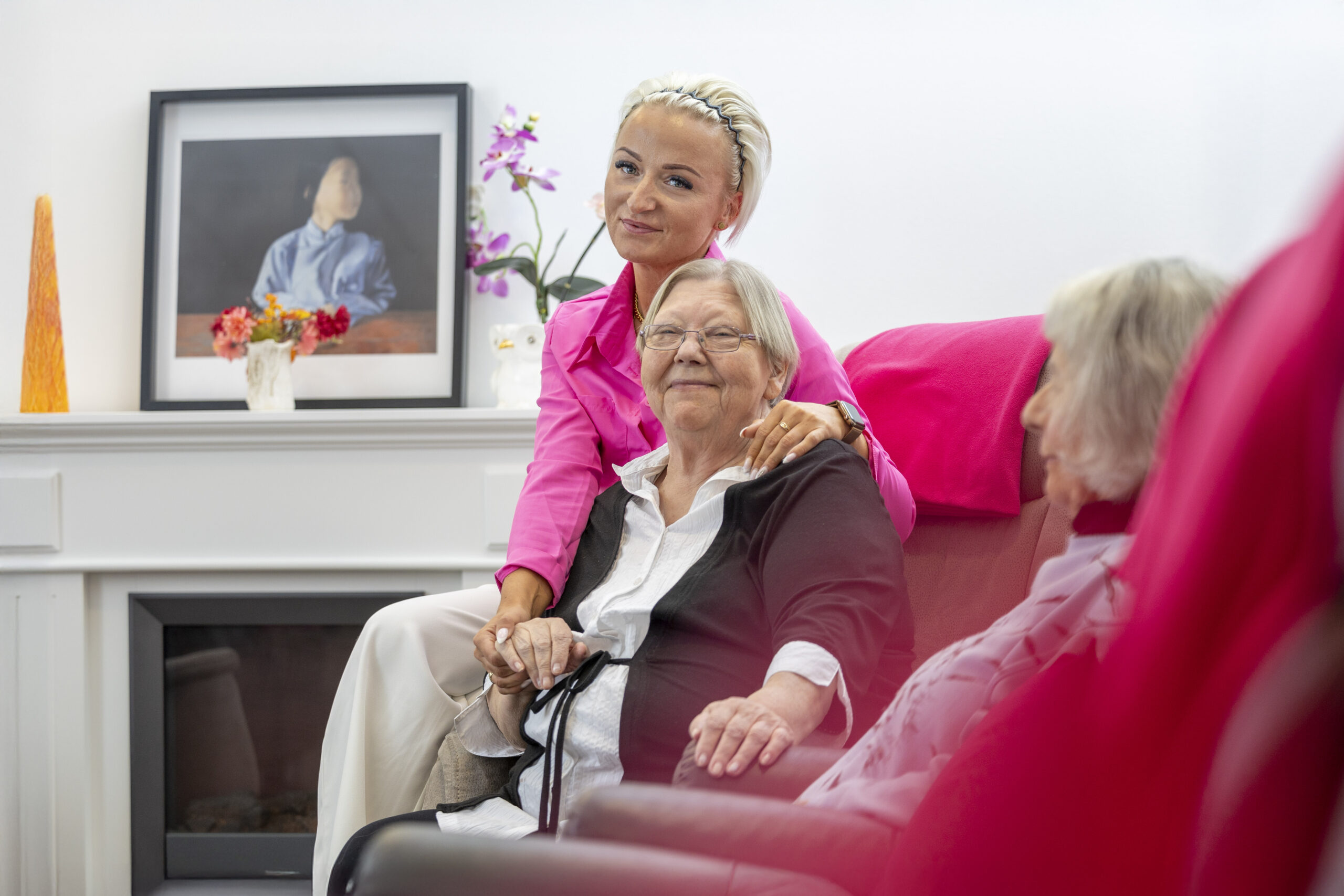 Mitarbeiterin hält die Hand einer Seniorin im Aufenthaltsbereich und spricht beruhigend mit ihr.