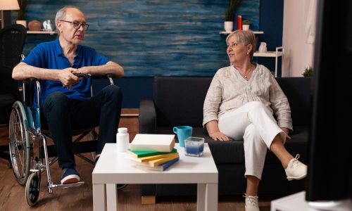 Mann im Rollstuhl und eine Frau sitzen entspannt im Aufenthaltsbereich und unterhalten sich – barrierefreie Sitzgruppe.